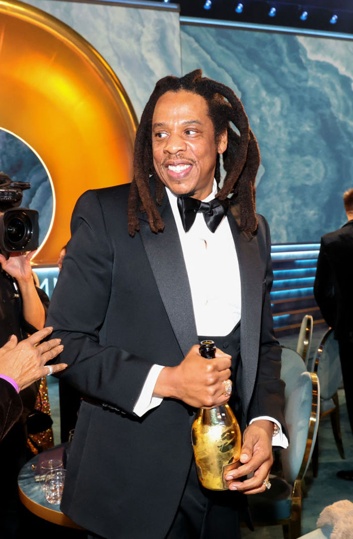 Jay-Z in a tuxedo holding champagne at an event, capturing a glimpse of his lavish lifestyle.