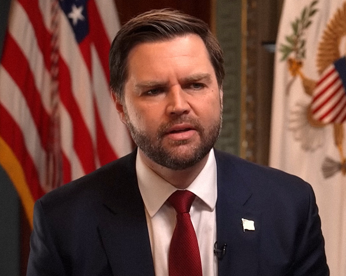 Man in a suit and red tie speaking, U.S. flags in the background. Man in a suit and red tie speaking, U.S. flags in the background.