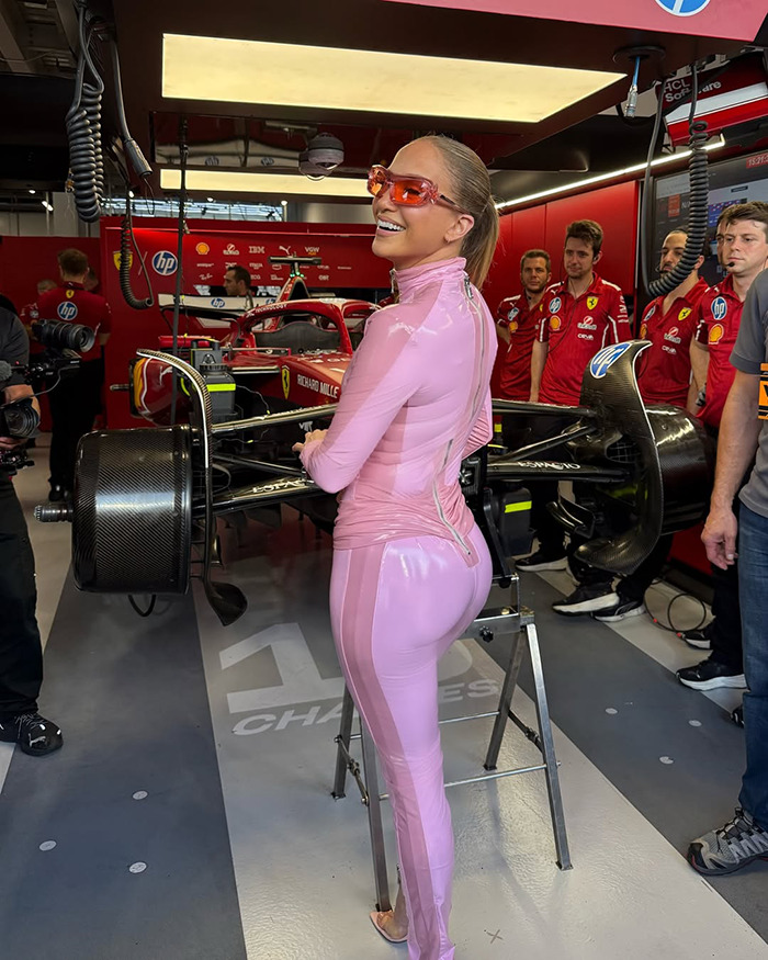 Person in pink catsuit at Saudi F1 race, standing by a car in the garage area, surrounded by team members. Person in pink catsuit at Saudi F1 race, standing by a car in the garage area, surrounded by team members.