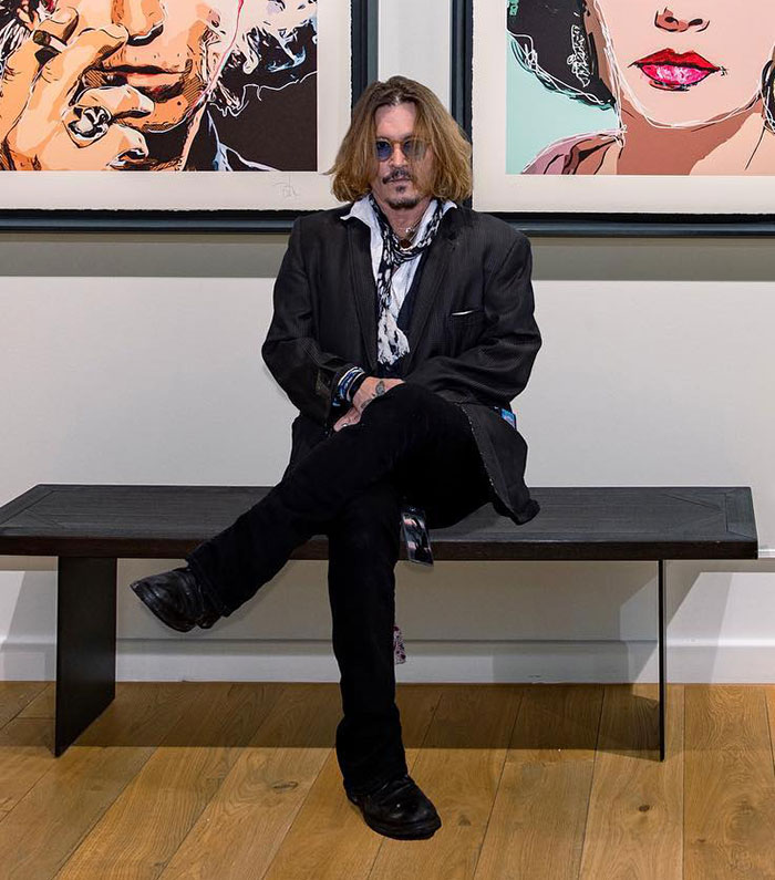 Man with sunglasses sits cross-legged on a bench in an art gallery, embodying a fresh Hollywood image. Man with sunglasses sits cross-legged on a bench in an art gallery, embodying a fresh Hollywood image.