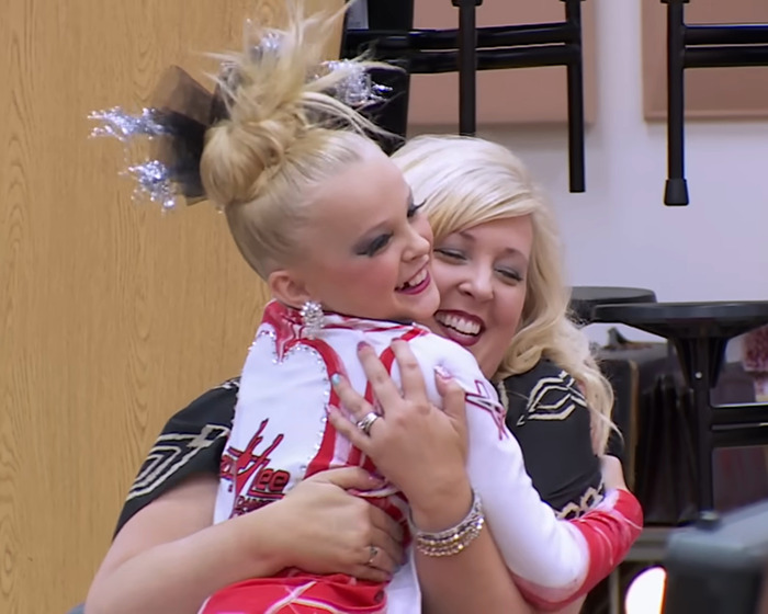 JoJo Siwa hugging a woman in a cheerful scene from 'Dance Moms,' amid recent controversy. JoJo Siwa hugging a woman in a cheerful scene from 'Dance Moms,' amid recent controversy.