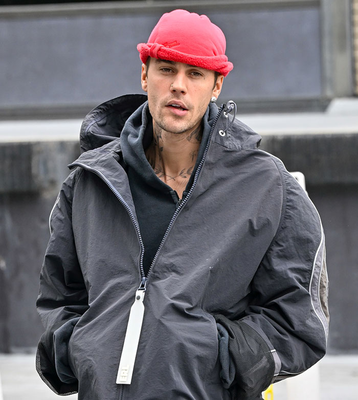 Young man in a red hat and black jacket outside, hands in pockets. Young man in a red hat and black jacket outside, hands in pockets.