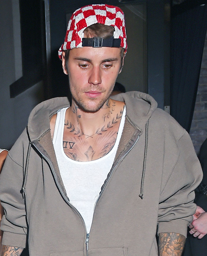 Justin Bieber in a casual outfit, wearing a red checkered hat, walking outside at night. Justin Bieber in a casual outfit, wearing a red checkered hat, walking outside at night.