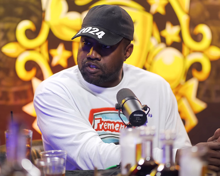 A man in a 2024 hat speaks into a microphone during an interview, with a colorful background. A man in a 2024 hat speaks into a microphone during an interview, with a colorful background.