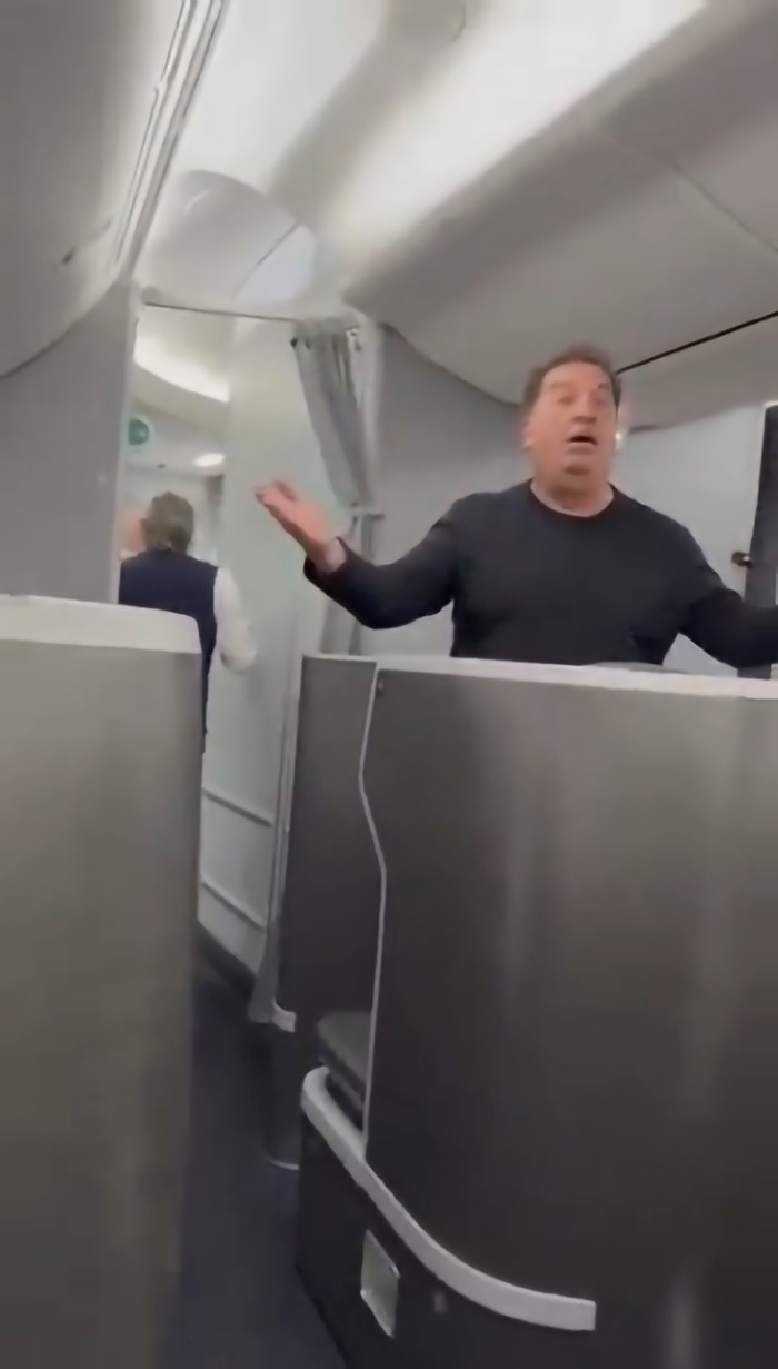 Man with raised arms inside airplane cabin during conflict related to flight delay and cockpit access attempt Man with raised arms inside airplane cabin during conflict related to flight delay and cockpit access attempt