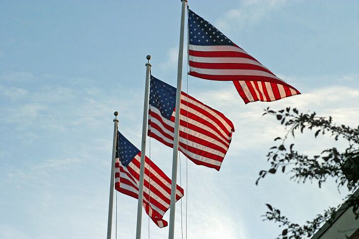 American flags waving on poles against a blue sky, highlighting cultural symbols noticed by non-Americans.