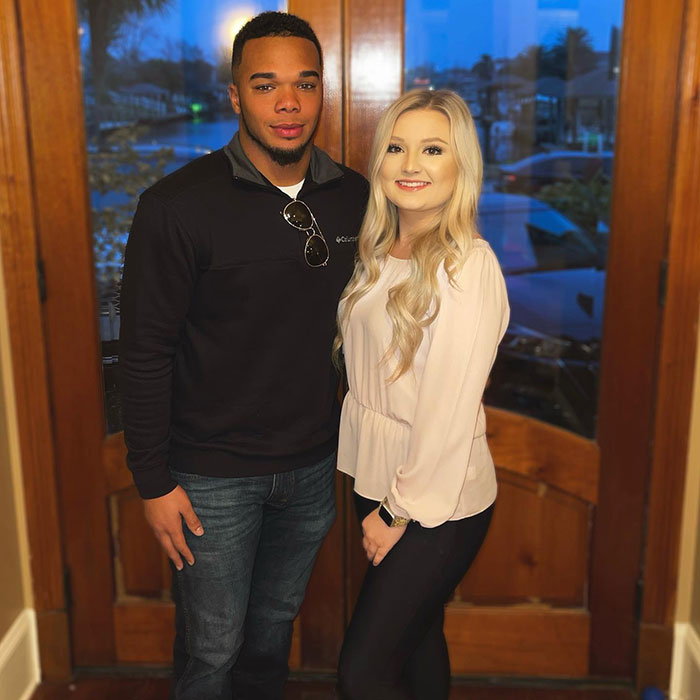 A couple standing together indoors, the man in a black jacket and the woman in a white blouse, smiling at the camera. A couple standing together indoors, the man in a black jacket and the woman in a white blouse, smiling at the camera.