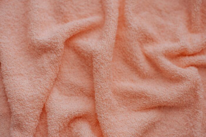 Peach-colored towel fabric close-up, showing texture and folds.