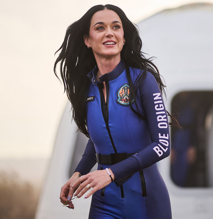 Singer in a Blue Origin suit, smiling and outdoors. Singer in a Blue Origin suit, smiling and outdoors.
