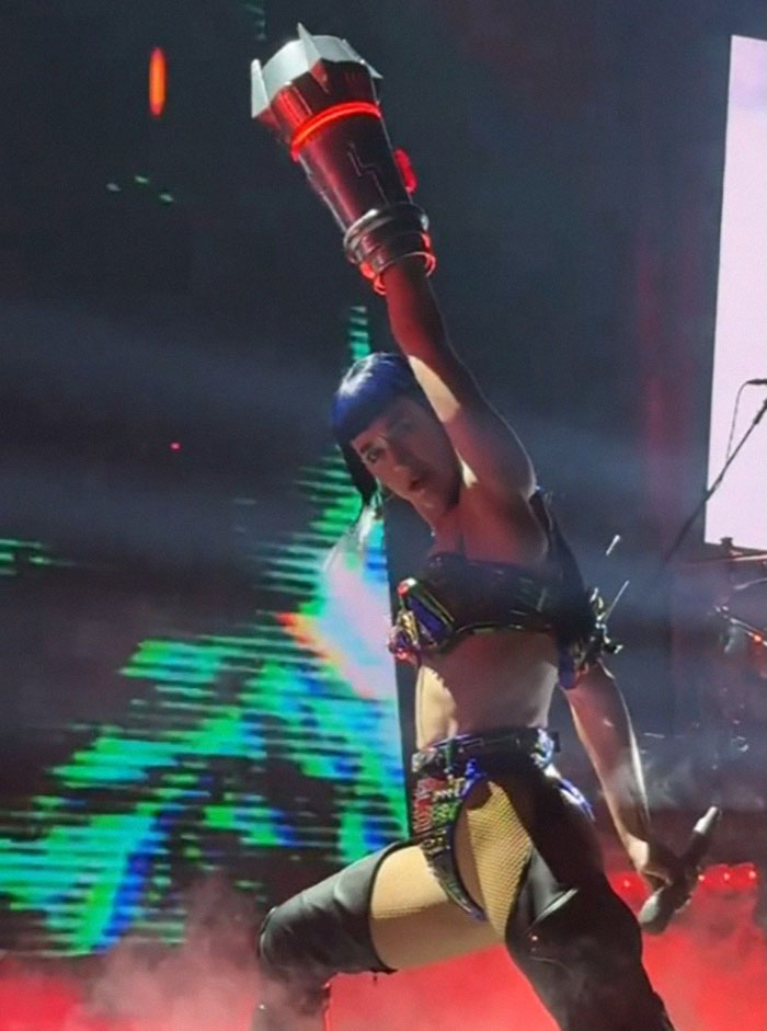 Singer performing on stage in futuristic attire, holding a microphone, with colorful lights in the background. Singer performing on stage in futuristic attire, holding a microphone, with colorful lights in the background.