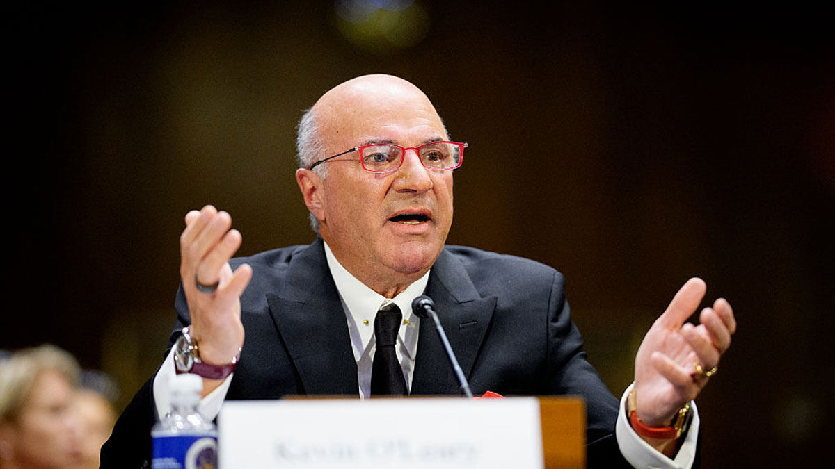 Kevin Ou2019Leary speaking at a panel, wearing a black suit and red glasses, discussing net worth and business growth.