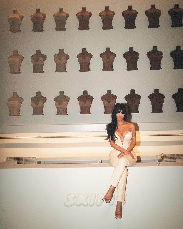 Woman in cream outfit posing amid mannequin wall display. Woman in cream outfit posing amid mannequin wall display.