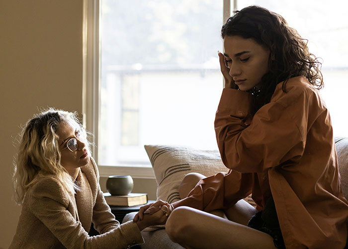 Two women discussing financial boundaries and bachelorette expenses in a living room setting. Two women discussing financial boundaries and bachelorette expenses in a living room setting.