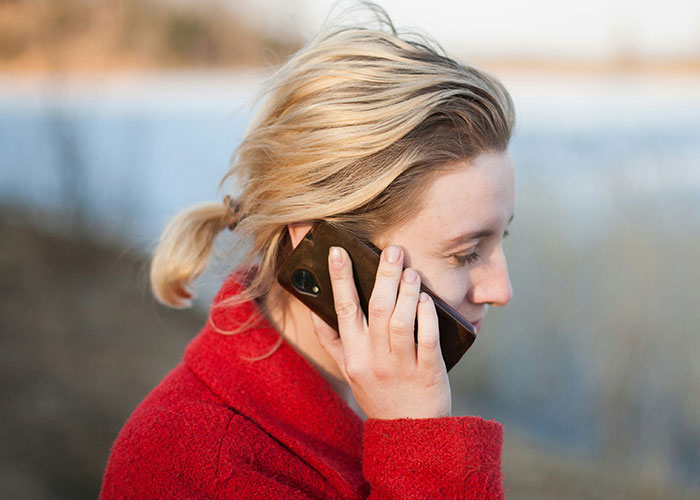Woman in a red coat talking on a phone by a lake, illustrating money boundaries in everyday conversations. Woman in a red coat talking on a phone by a lake, illustrating money boundaries in everyday conversations.