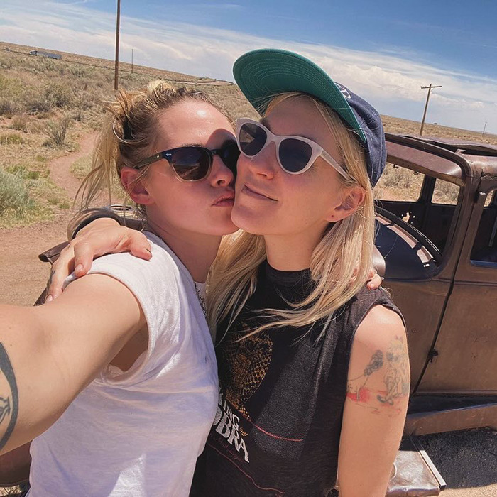 Lovebirds share a kiss outdoors, wearing sunglasses and casual attire, posing next to a vintage car. Lovebirds share a kiss outdoors, wearing sunglasses and casual attire, posing next to a vintage car.