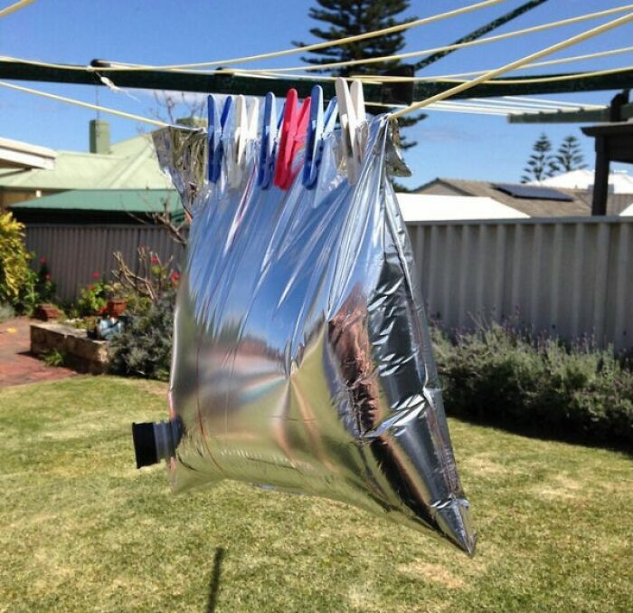 Silver bag filled with water hanging on a clothesline with pegs, a super normal thing in the country backyard setting.