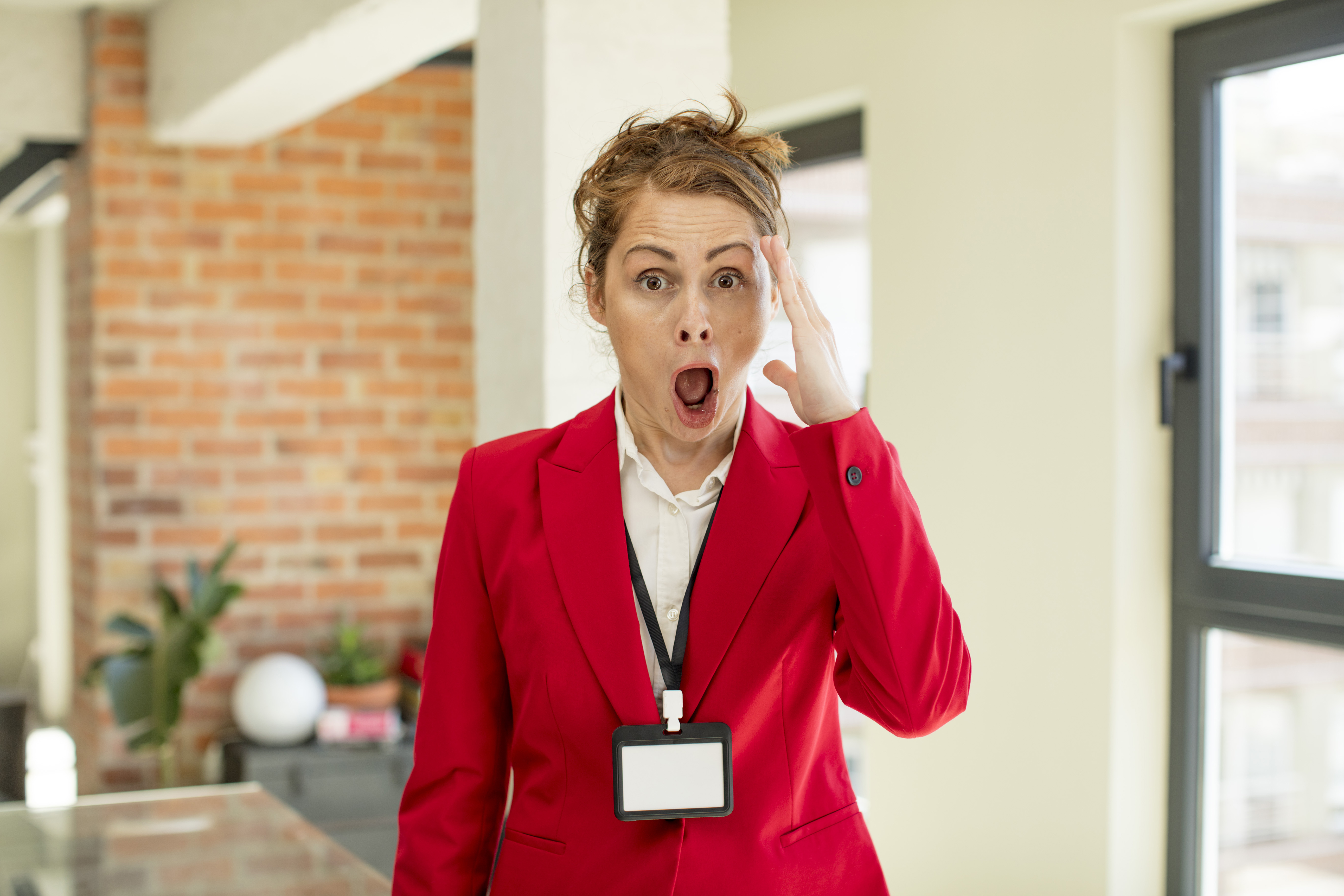 Event manager in a red suit looking shocked with hand on forehead indoors. Event manager in a red suit looking shocked with hand on forehead indoors.
