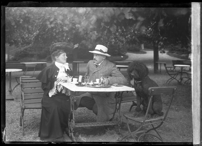 Black and white rare photograph of a man and woman in vintage clothing with a dog at a garden table from glass negatives.