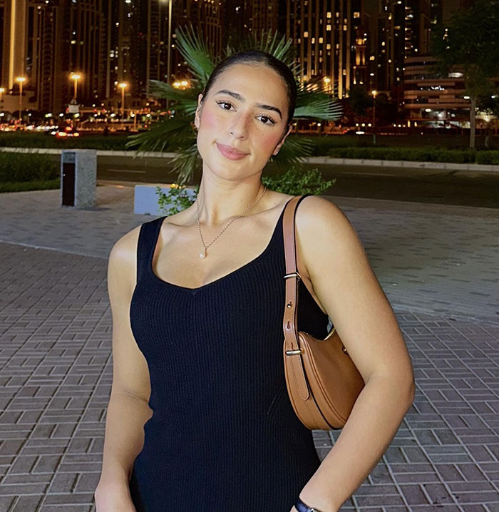 Woman in a black dress smiling at night with city lights in background, holding a brown purse. Woman in a black dress smiling at night with city lights in background, holding a brown purse.