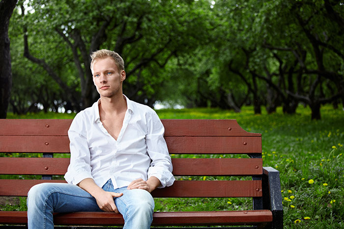 Young man sitting on a park bench in a peaceful setting, wearing a white shirt and jeans, surrounded by lush greenery. Young man sitting on a park bench in a peaceful setting, wearing a white shirt and jeans, surrounded by lush greenery.