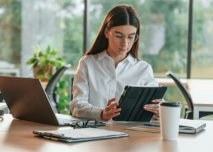 Employee in office with tablet and laptop, reflecting on team dynamics and leadership decisions. Employee in office with tablet and laptop, reflecting on team dynamics and leadership decisions.