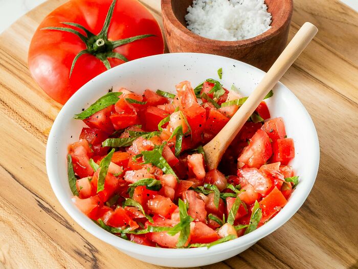 Bowl of tomato salad with basil and a wooden spoon, showcasing fresh ingredients with absolute confidence in presentation.