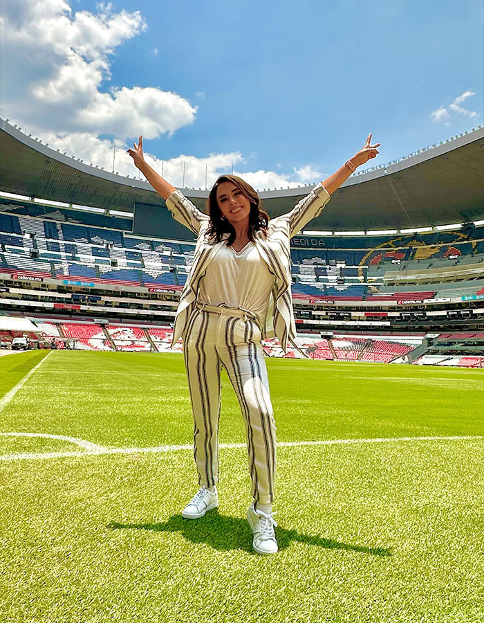 Female reporter stands on a soccer field, arms raised, smiling widely at the stadium. Female reporter stands on a soccer field, arms raised, smiling widely at the stadium.