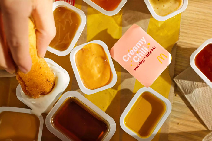 Hand dipping McDonald's chicken strip into sauces on a table. Hand dipping McDonald's chicken strip into sauces on a table.