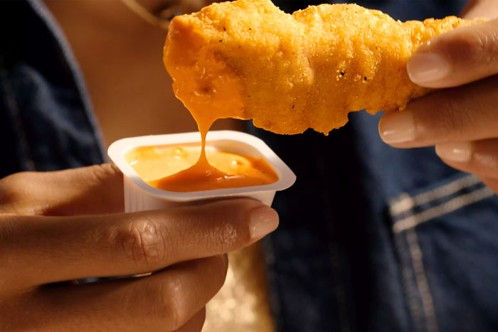 Close-up of a person dipping a McDonald's chicken strip into orange sauce. Close-up of a person dipping a McDonald's chicken strip into orange sauce.