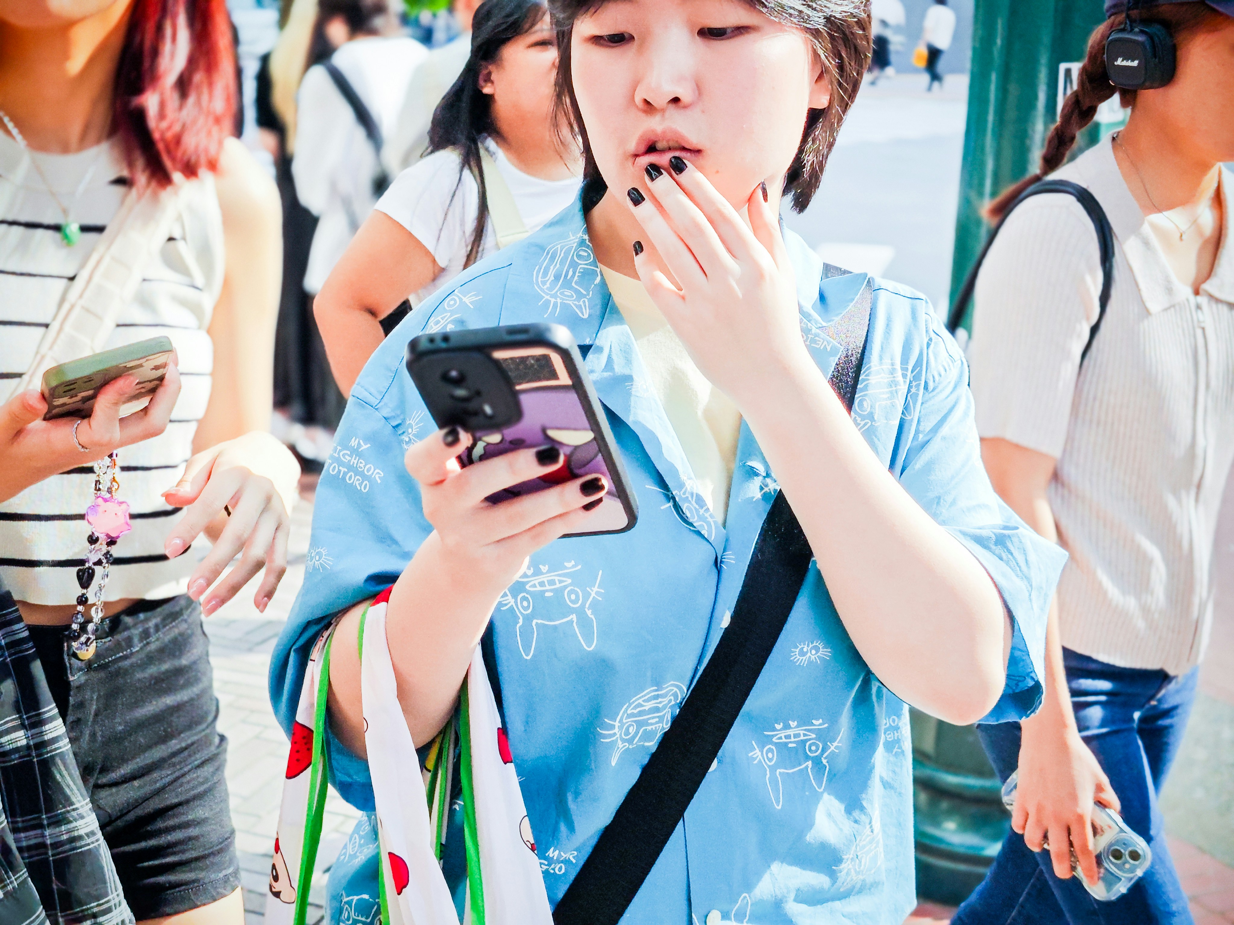 Woman in a blue shirt holding an expensive phone case while walking in a crowd outdoors. Woman in a blue shirt holding an expensive phone case while walking in a crowd outdoors.