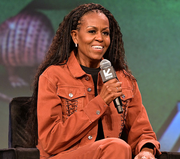 Michelle Obama speaking at an event in a brown outfit, addressing divorce rumors with a microphone in hand. Michelle Obama speaking at an event in a brown outfit, addressing divorce rumors with a microphone in hand.