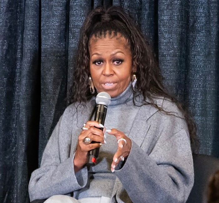 Michelle Obama addresses audience, holding a microphone, in a grey outfit, discussing divorce rumors. Michelle Obama addresses audience, holding a microphone, in a grey outfit, discussing divorce rumors.
