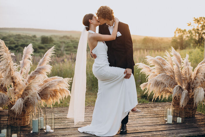 Bride and groom kissing outdoors surrounded by pampas grass, capturing the joy of weddings and new generational views. Bride and groom kissing outdoors surrounded by pampas grass, capturing the joy of weddings and new generational views.