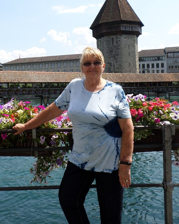 Woman standing by flowers with a historic tower in the background, wearing sunglasses and a tie-dye shirt. Woman standing by flowers with a historic tower in the background, wearing sunglasses and a tie-dye shirt.