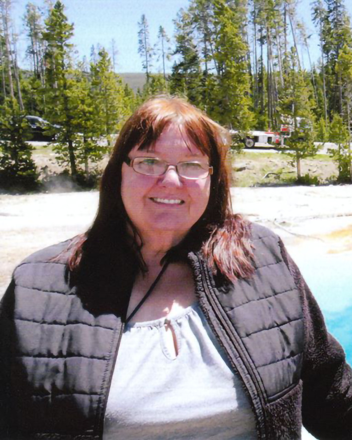 Woman outdoors wearing glasses and a black jacket, with trees in the background. Woman outdoors wearing glasses and a black jacket, with trees in the background.