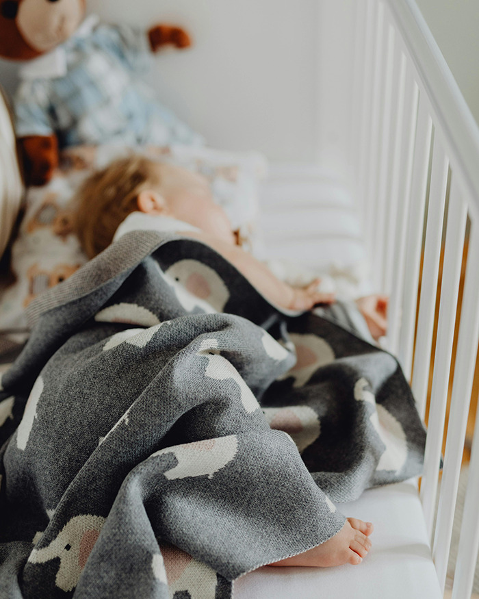 Baby sleeping in a crib with a grey blanket featuring animal designs. Baby sleeping in a crib with a grey blanket featuring animal designs.