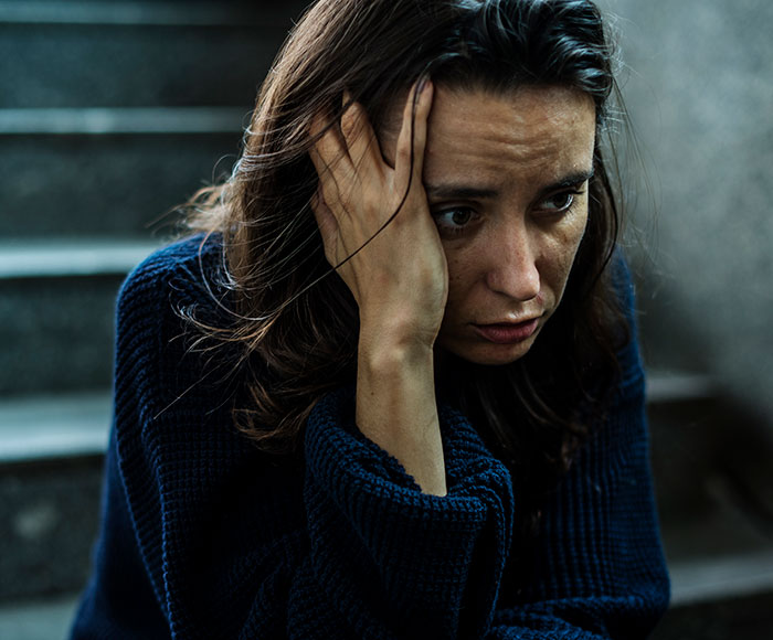 A woman appearing distressed, holding her head while sitting on stairs, reflecting on money and family apartment share issues. A woman appearing distressed, holding her head while sitting on stairs, reflecting on money and family apartment share issues.