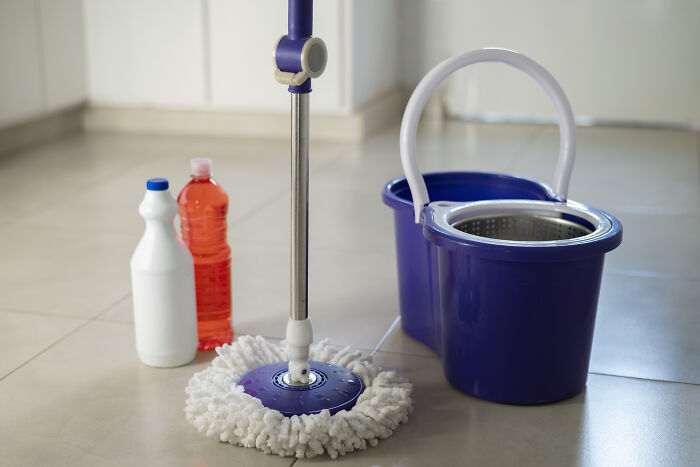 Cleaning supplies on the floor, featuring a mop, bucket, and two bottles, part of an everyday cleaning setup.
