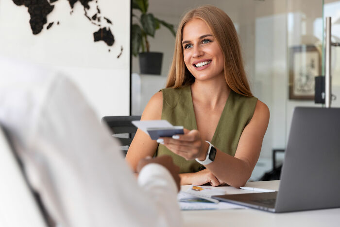 Smiling woman handing a credit card across a desk, embodying a normal social interaction in a professional setting.