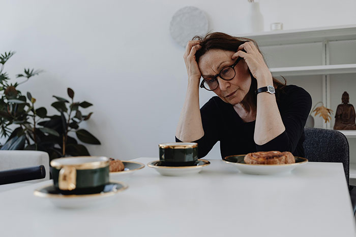 A woman looking stressed and concerned, sitting at a table with coffee cups, reflecting family dynamics and expectations. A woman looking stressed and concerned, sitting at a table with coffee cups, reflecting family dynamics and expectations.