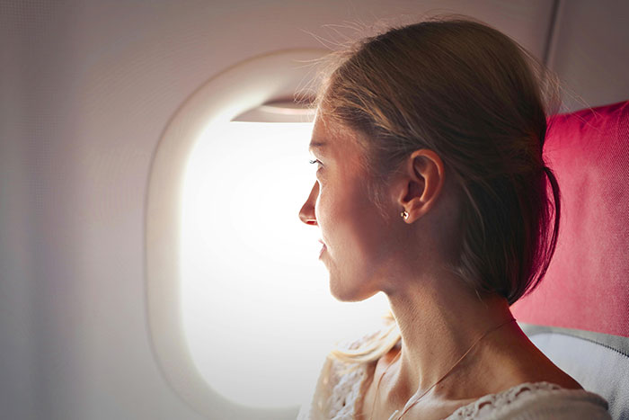 Woman on airplane, gazing out window, reflecting on distance from family and help with child, feeling introspective. Woman on airplane, gazing out window, reflecting on distance from family and help with child, feeling introspective.