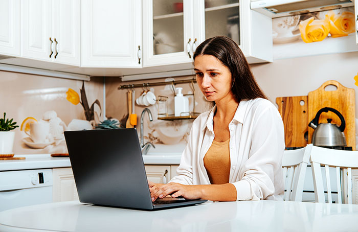 Woman on maternity leave types on laptop in kitchen, focused on task. Woman on maternity leave types on laptop in kitchen, focused on task.
