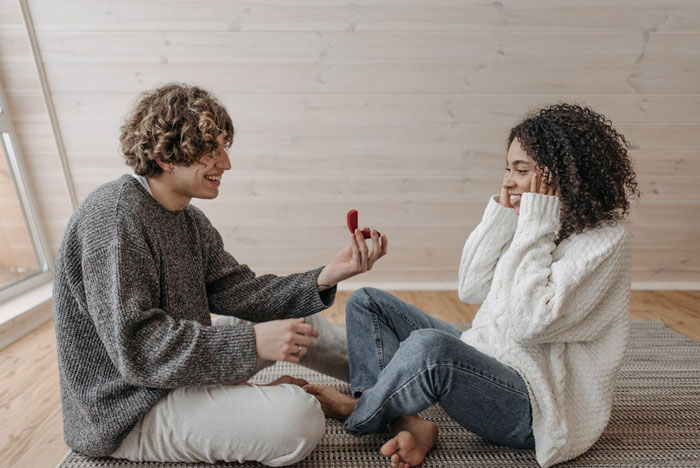 Couple sitting on floor, man proposing with a ring, discussing hyphenated last names after marriage. Couple sitting on floor, man proposing with a ring, discussing hyphenated last names after marriage.