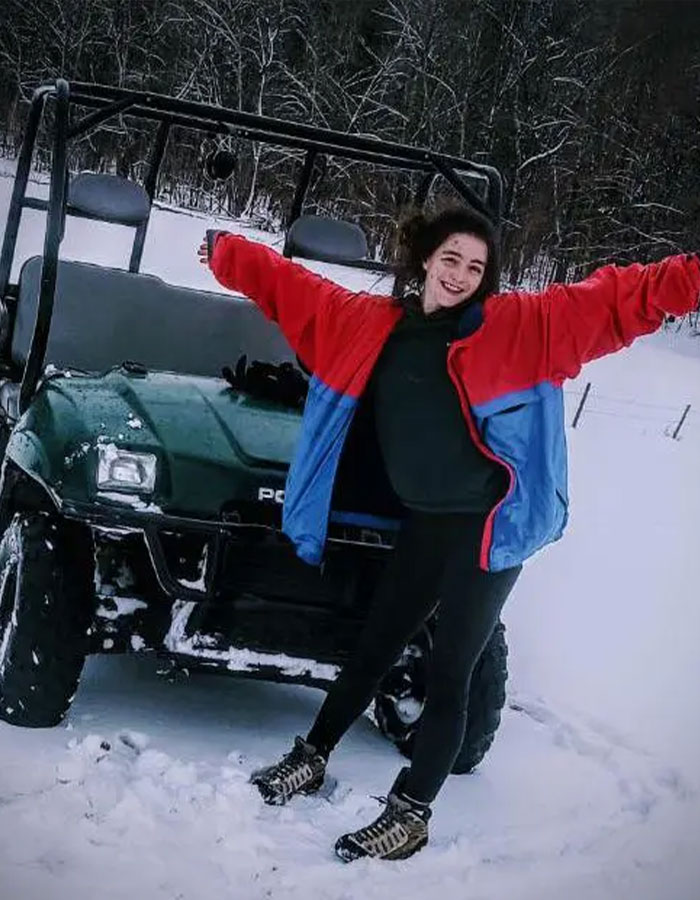 Former child star in snow, smiling next to a snow-covered vehicle, wearing a red and blue jacket. Former child star in snow, smiling next to a snow-covered vehicle, wearing a red and blue jacket.