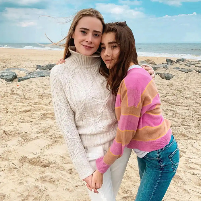 Two people on a beach, one in a cream sweater and the other in a pink striped sweater, embracing with the ocean behind. Two people on a beach, one in a cream sweater and the other in a pink striped sweater, embracing with the ocean behind.