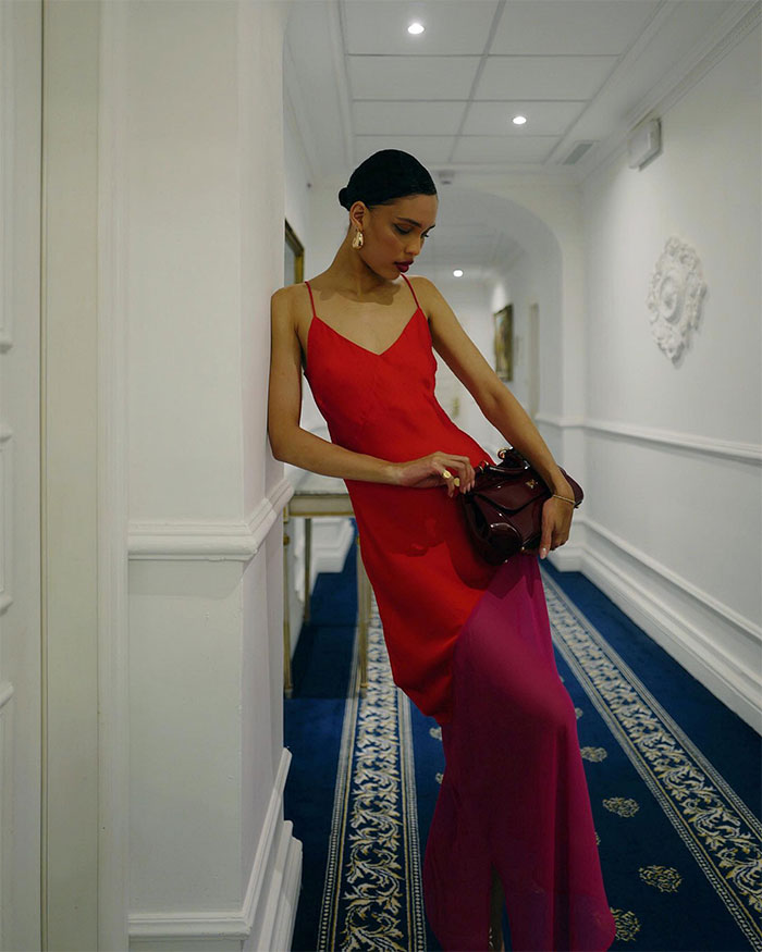Nara Smith in elegant red dress, leaning against a wall in a bright hallway, illustrating calm composure.