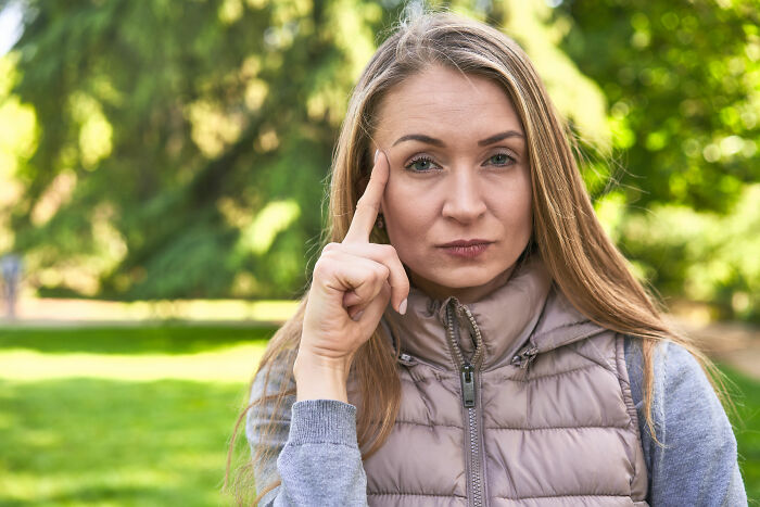 Woman in a park looking assertive, touching her temple, related to a neighbor dispute about pets. Woman in a park looking assertive, touching her temple, related to a neighbor dispute about pets.