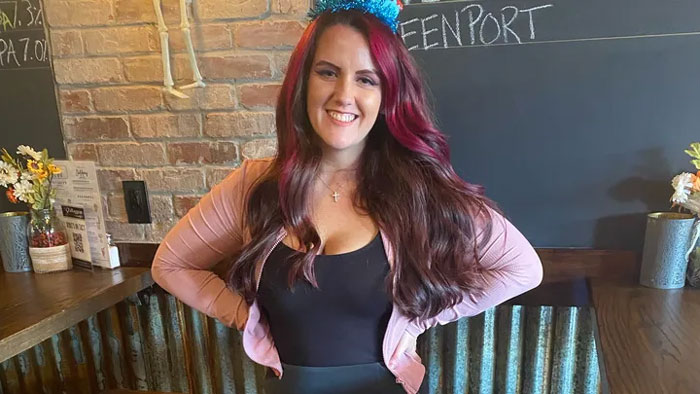 A woman with long red hair and a black outfit smiling indoors, relevant to New England serial assassination horror news. A woman with long red hair and a black outfit smiling indoors, relevant to New England serial assassination horror news.