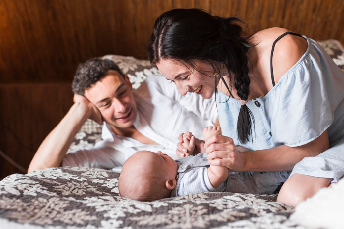 A couple enjoying a peaceful moment with their newborn in a cozy bedroom setting. A couple enjoying a peaceful moment with their newborn in a cozy bedroom setting.