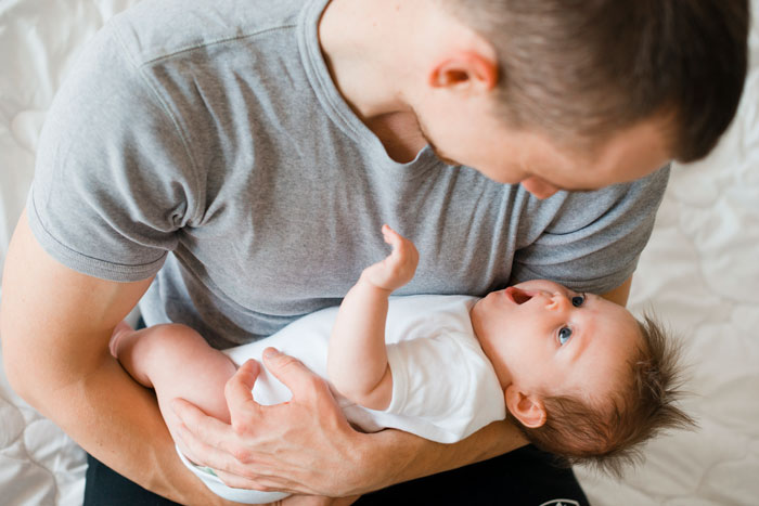 Father holding newborn baby, smiling in a cozy bedroom setting. Father holding newborn baby, smiling in a cozy bedroom setting.